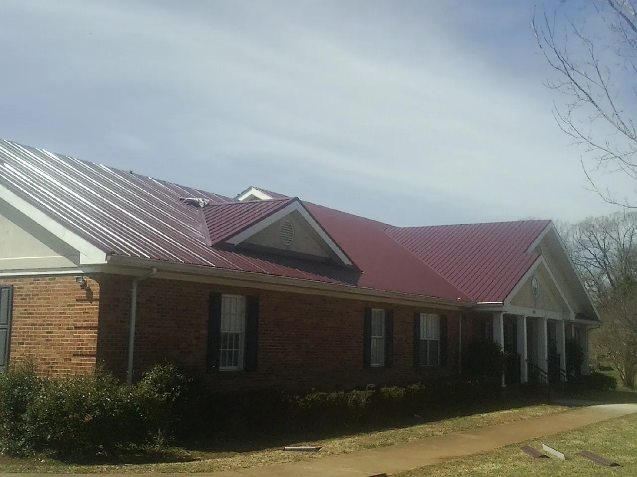 Red metal roof with gabled entries on a long brick building, from a Hail Damage Roof Repair job in Seymour