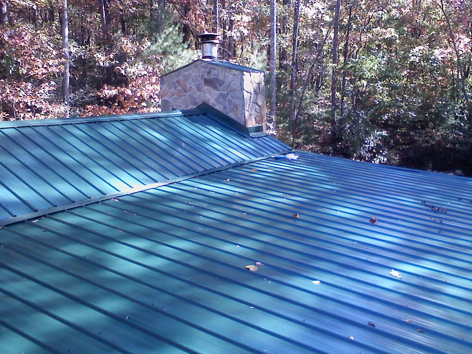 New green metal roof and stone chimney surrounded by autumn woods in Seymour