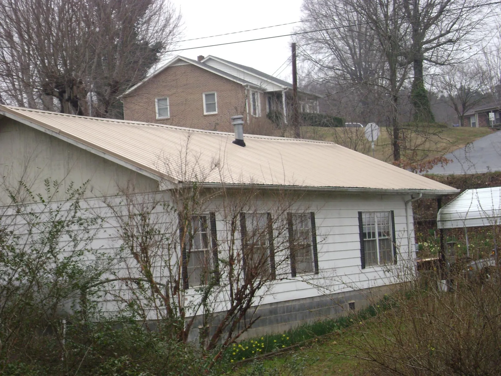 Tan metal roof on a white sided house set into a hillside — Commercial Roofing by Roofing Brothers in Seymour
